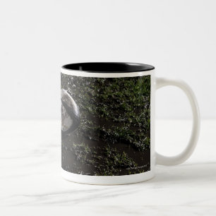 Muddy rugby ball sitting on a chewed up grass Two-Tone coffee mug
