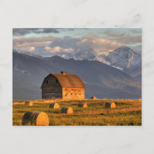 Old barn framed by hay bales and dramatic postcard