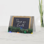 Peace On Earth sign on black chalkboard Holiday Card<br><div class="desc">Christmas greeting sign on black chalkboard with glowing holiday lights and green garland</div>