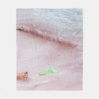 Person's foot beside green shovel on seashore fleece blanket
