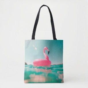 Pink flamingo swim ring on body of water in summer tote bag