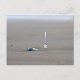 plastic fork sticking in sandy beach beside postcard