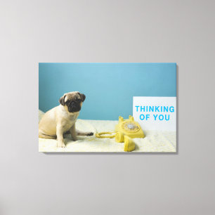 Pug puppy sitting on bed next to phone and canvas print