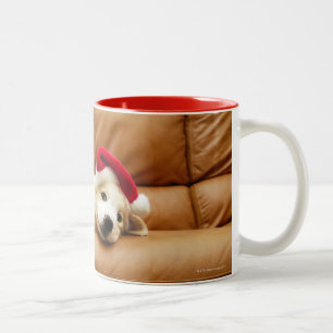 Puppy wears a christmas hat and lying on sofa Two-Tone coffee mug