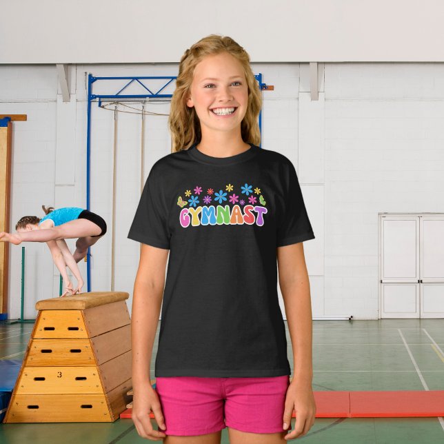 Retro Gymnast T-shirt | Gymnastics themed T-shirt  (A young girl wearing gymnast black t-shirt with flower power style retro design. Gymnasium behind.)