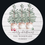 Rustic Christmas Pine Trees Snow Family Name Classic Round Sticker<br><div class="desc">A warm rustic Christmas tree farm theme with festive ornaments,  and merry Christmas script typography overlay,  on a whitewashed shiplap wood background with falling snow. For a soft earthy homey rustic vibe holiday sticker with modern typography.</div>