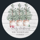 Rustic Christmas Pine Trees Snow Family Name Classic Round Sticker<br><div class="desc">A warm rustic Christmas tree farm theme with festive ornaments,  and merry Christmas script typography overlay,  on a whitewashed shiplap wood background with falling snow. For a soft earthy homey rustic vibe holiday sticker with modern typography.</div>