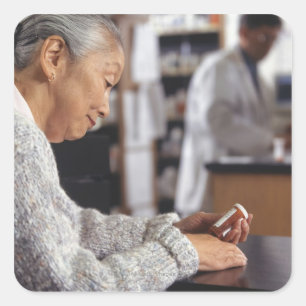 Senior woman in pharmacy reading medicine bottle square sticker