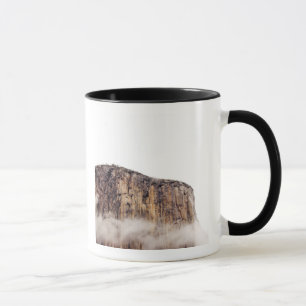 Sheer cliff rising above clouds mug