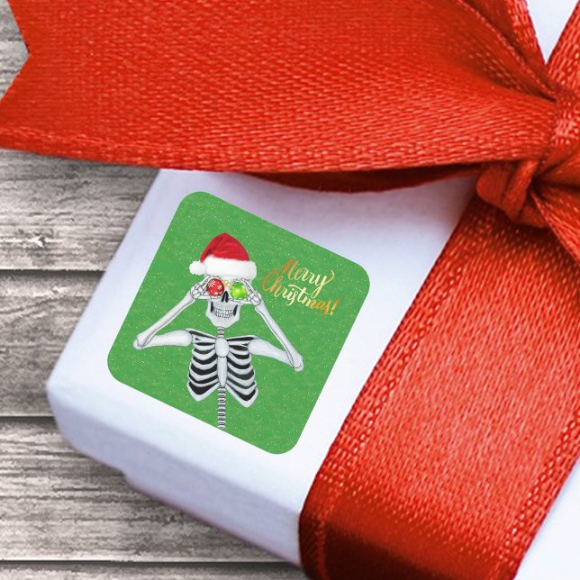 Smiling Christmas Skeleton Ornament Eyes on Green Square Sticker (Funny Merry Christmas Skeleton ornament eyes Santa Hat on green with gold flecks paper sticker.)