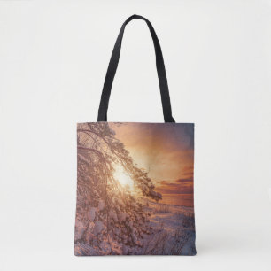 Sunset over sea and snowy pine tree tote bag