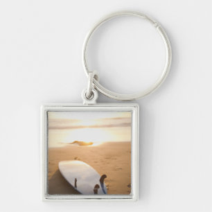 Surfboard laying on beach at sunset key ring