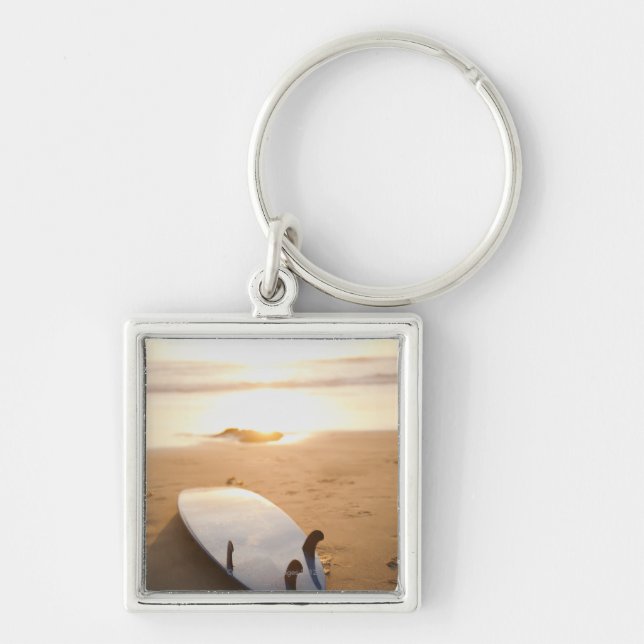 Surfboard laying on beach at sunset key ring (Front)