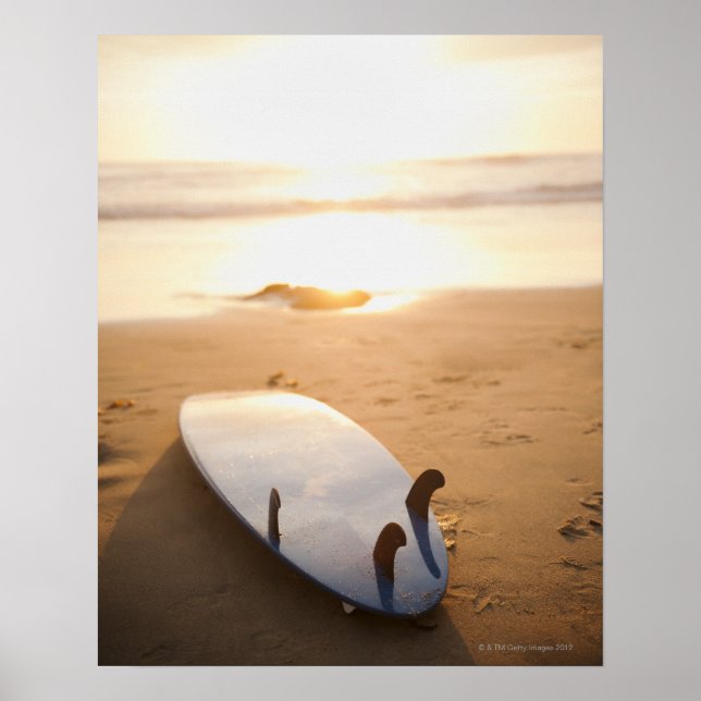 Surfboard laying on beach at sunset poster (Front)