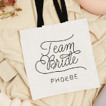Team Bride Modern Script Gold Wedding Name Tote Bag<br><div class="desc">This modern tote bag with a minimalist casual chic script calligraphy design reading TEAM BRIDE as well as the custom name of your maid of honor or bridesmaid features clean lines to create a sleek and sophisticated appearance. The understated style with the little printed gold heart detail adds a touch...</div>