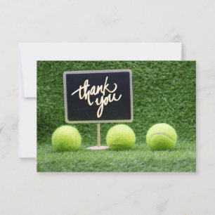 Tennis ball is on green grass with chalkboard thank you card