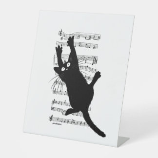 The cat hangs on musical notes pedestal sign