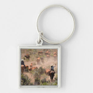 Three cowboys and cowgirls driving cattle key ring