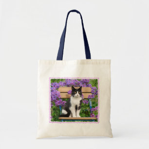 Tuxedo cat sitting on a garden chair with flowers tote bag