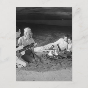 Two couples on beach sitting around campfire postcard