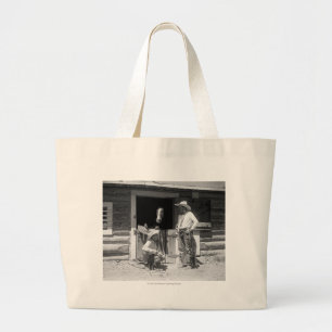 Two cowboys standing next to a barn with a horse large tote bag