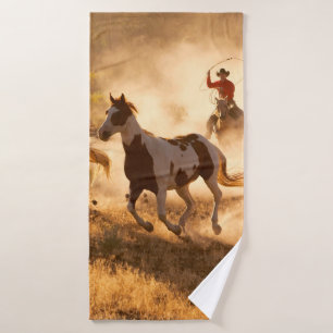 Two western cowboys riding horses, roping wild hor bath towel