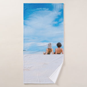 Two women lying on white sand facing beach under b bath towel