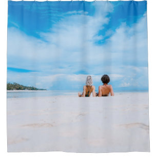 Two women lying on white sand facing beach under b shower curtain