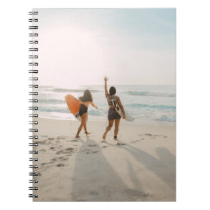 Two women walking towards the ocean carrying surfb notebook