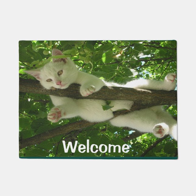 Welcome Cat Doormat ( A white kitten lying on a tree branch amidst lush green foliage.)