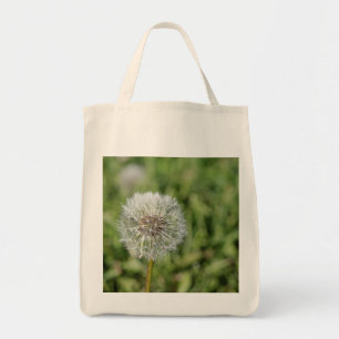 White dandelion flower on green grass tote bag