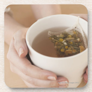 Woman holding cup with chamomile tea coaster