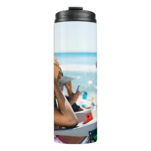 Woman lying on sun lounger covering her face with  thermal tumbler