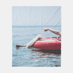 Woman on an inflatable float in the ocean pointing fleece blanket