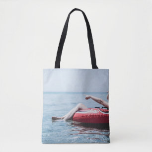 Woman on an inflatable float in the ocean pointing tote bag