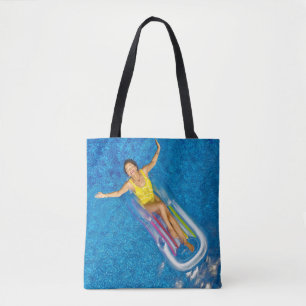 Woman riding on plastic floating buoy on body of w tote bag