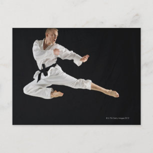 Young man performing karate kick on black postcard