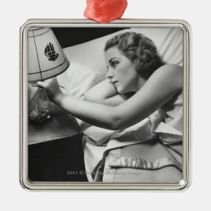 Young woman lying on bed turning off lamp on metal tree decoration