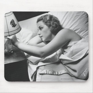 Young woman lying on bed turning off lamp on mouse mat
