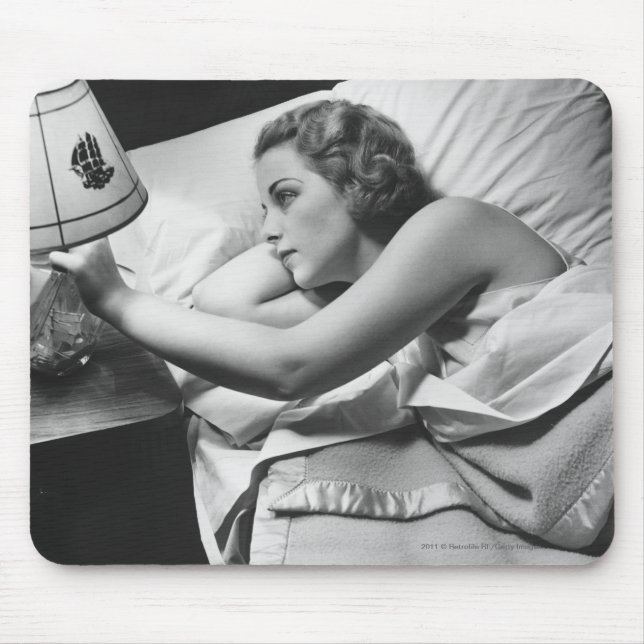 Young woman lying on bed turning off lamp on mouse mat (Front)