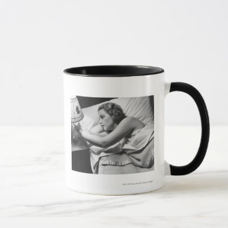 Young woman lying on bed turning off lamp on mug